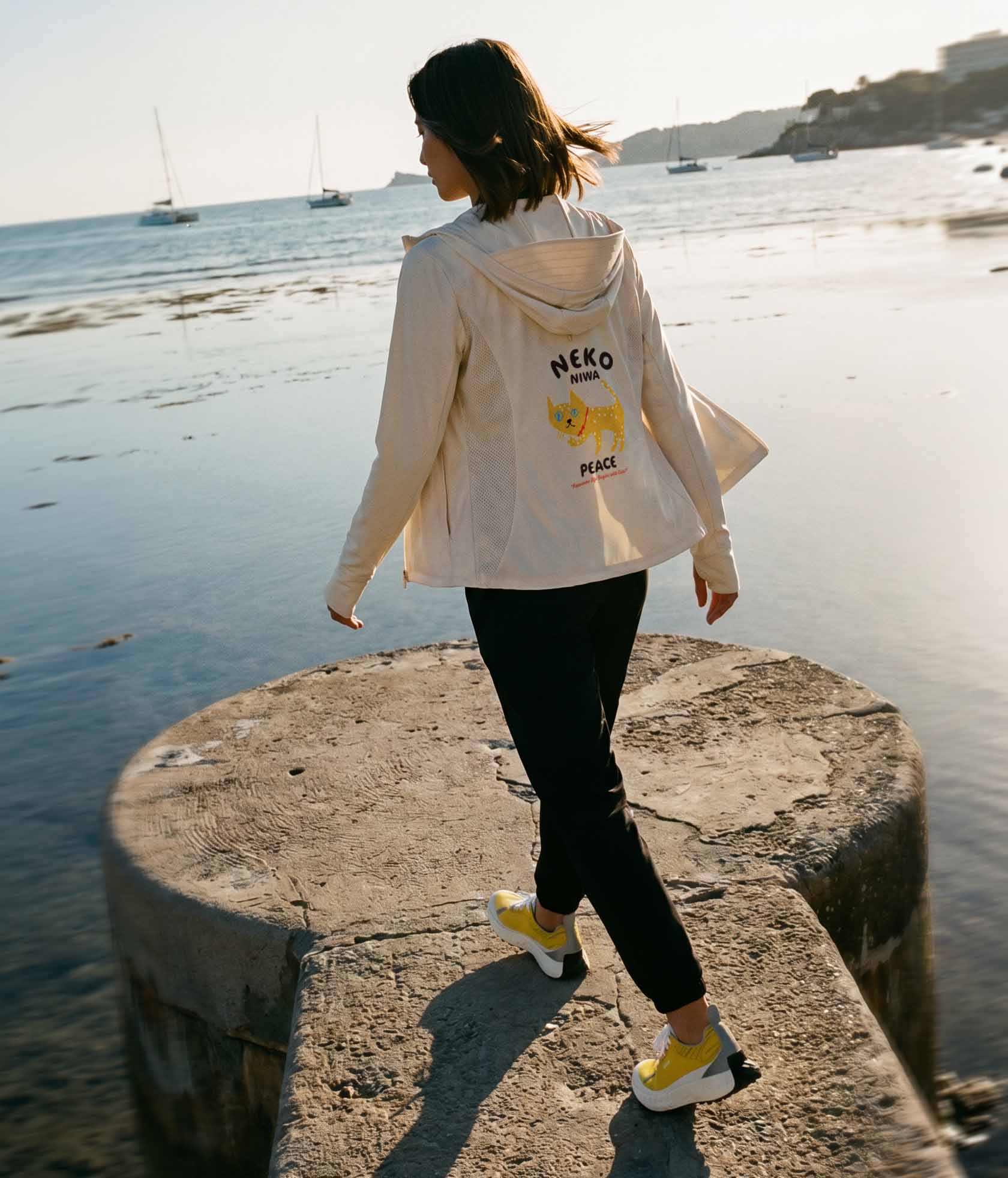 海辺の岩場を歩く女性・ベージュのNEKONI UV HOODIE着用