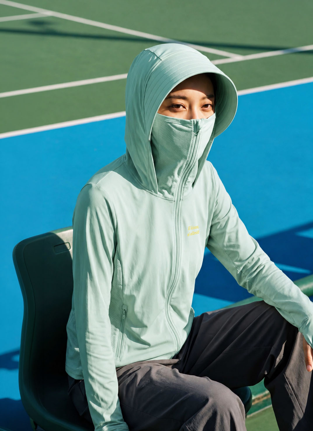テニスコートで面マスク姿・グリーンのNEKONI UV HOODIE着用